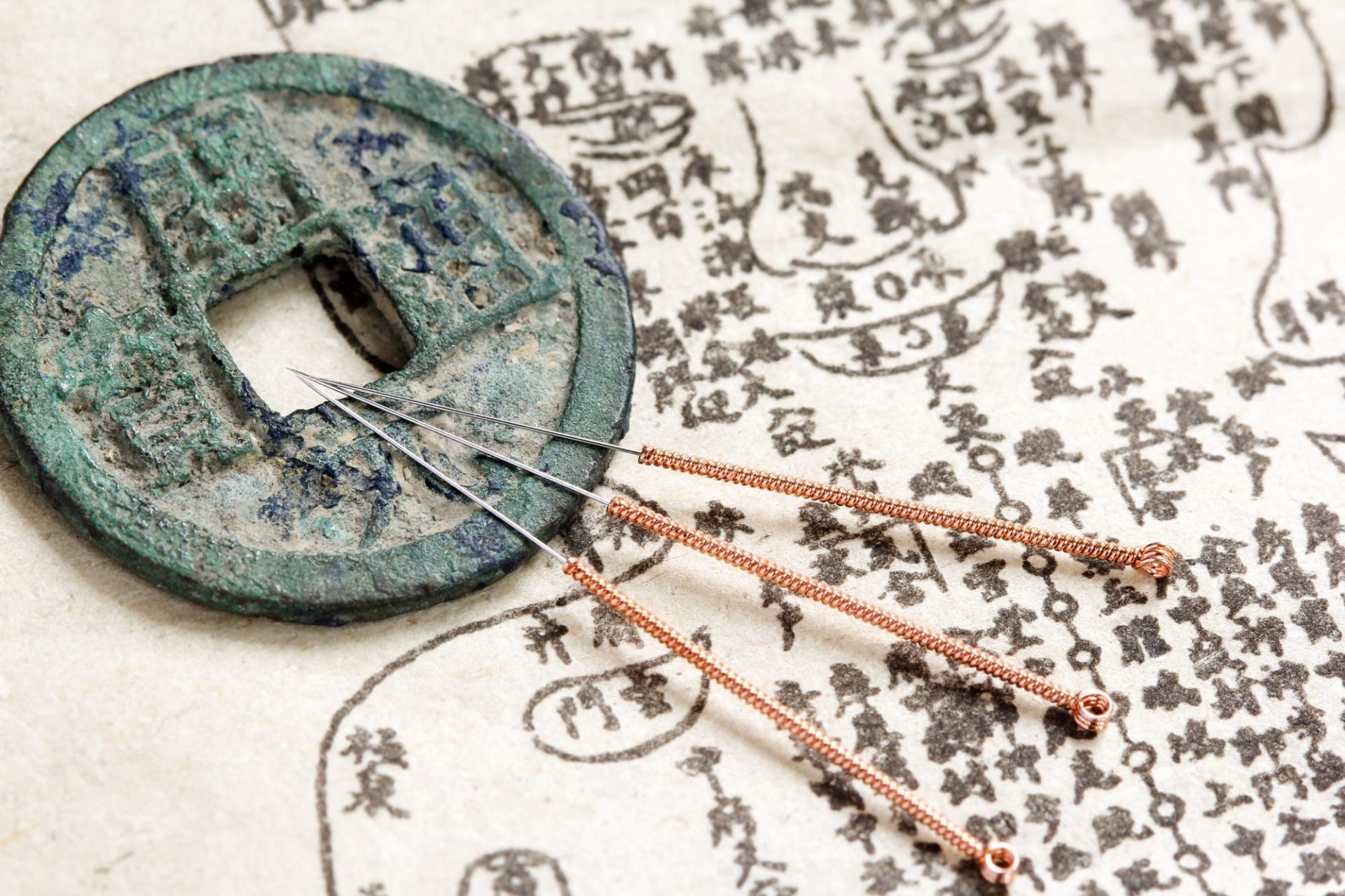 Acupuncture needles and an antique Chinese coin resting on a traditional Chinese medicine meridian chart