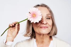 A woman holding a soft pink flower beside her face, glowing complexion